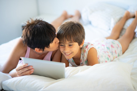 Middle age mother with her eight years daughter using digital tablet in bedroom