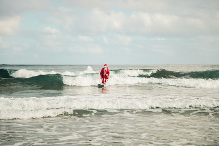 Young man surfer dressed as Santa Claus on the beach