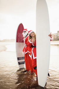 two surfers dressed as Santa Claus on the beach
