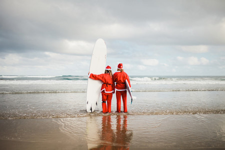 two surfers dressed as Santa Claus on the beach