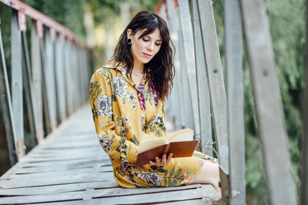 Young woman reading a book on a rural bridge