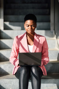 Black woman sitting on urban steps working with a laptop computer