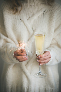 Woman in sweater holding champagne and sparkler in hands
