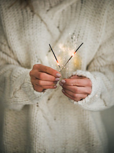 Woman in sweater holding Christmas sparklers in hands  close up