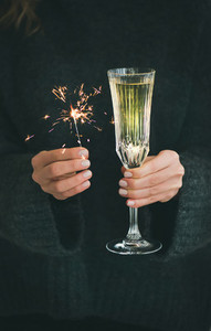 Woman in grey sweater holding sparklers and glass of champagne