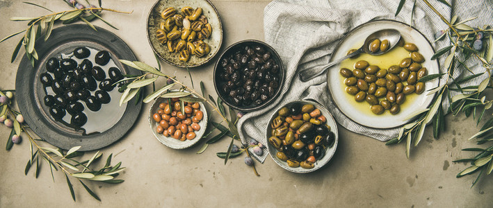 Mediterranean pickled olives and olive tree branches on grey background