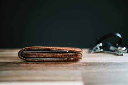 Brown leather wallet and keys on a wooden table with black background
