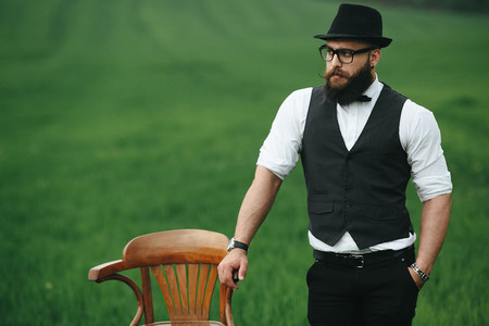 A man with a beard  thinking in a field near chair