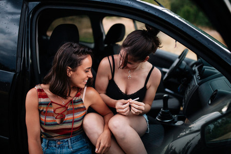 Two young lesbians rolling an handmade cigarette in the car