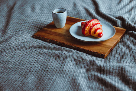 Cherry croissant with a cup of espresso on a wooden tray in a bed  Copy space