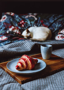 Cherry croissant with a cup of espresso on a wooden tray in a bed  The concept of cozy morning at home