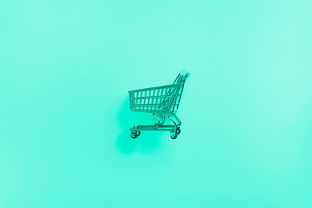 Shopping cart on mint color background  Minimalism style  Shop trolley at supermarket  Trendy green and turquoise color  Sale  discount  shopaholism concept  Consumer society trend