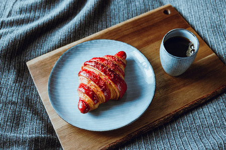Cherry croissant with a cup of espresso on a wooden tray in a bed