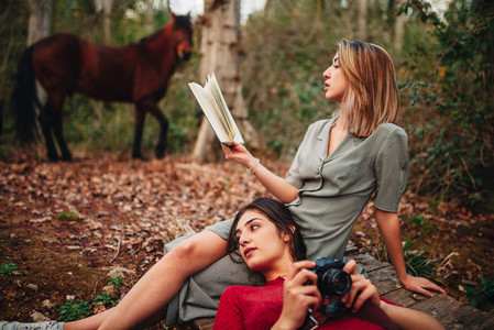 Young women reading a book and taking photos in the forest