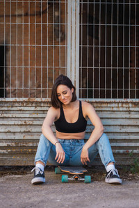 Young woman sitting on her skate in an old industrial street