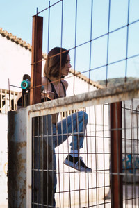 Young woman skater trying to climb over the fence