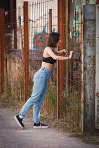 Young woman skater look inside through a fence