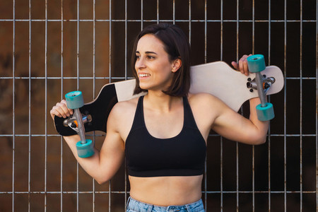 Young woman skater smiling holding her longboard behind her head