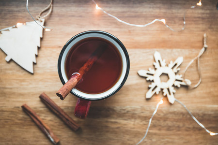 Top view of black tea with cinnamon in a red mug among winter decor and lights Cozy winter time still life