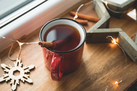 Black tea with cinnamon in a red mug among winter decor and lights Cozy winter time still life