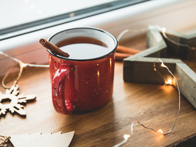 Black tea with cinnamon in a red mug among winter decor and lights Cozy winter time still life