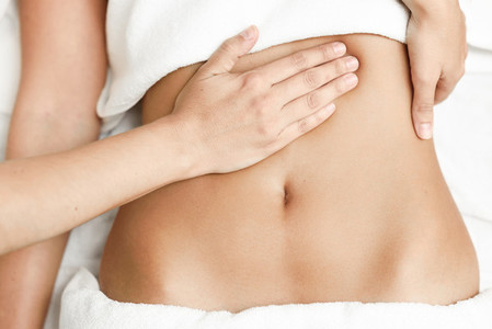 Hands massaging female abdomenTherapist applying pressure on belly