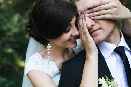 Charming bride closes eyes to her husbend from behind