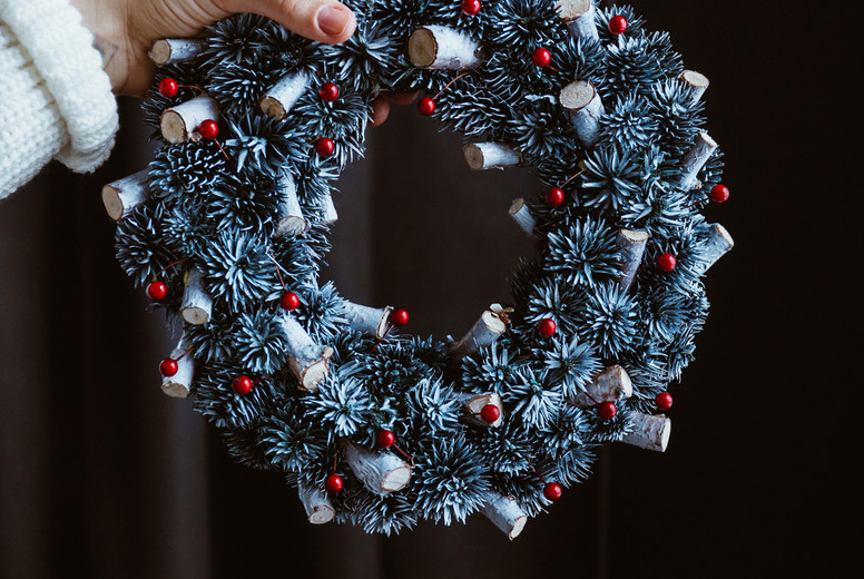 Womans hand in a winter white sweater holds a Christmas holiday wreath over dark background.