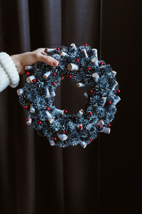 Womans hand in a winter white sweater holds a Christmas holiday wreath over dark background