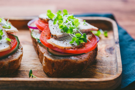 Sandwiches with turkey meat and fresh vegetables served with microgreens on a wooden plate The concept of healthy and diet eating