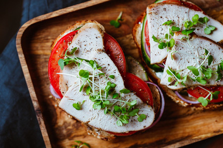 Sandwiches with turkey meat and fresh vegetables served with microgreens on a wooden plate Top view flat lay macro food photography
