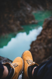 Feet of traveler in boots sitting over river canyon