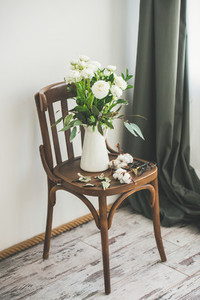 Spring white buttercup flowers in enamel jug on vintage chair
