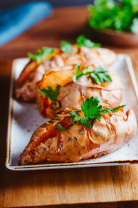 Baked three sweet potatoes with fresh parsley on a white ceramic dish  Healthy veggie dinner or lunch