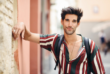 Attractive young man with dark hair and modern hairstyle wearing casual clothes outdoors