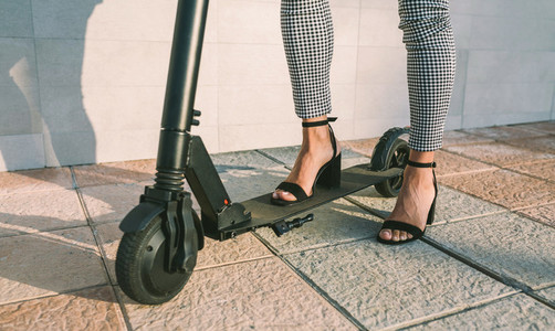 Unrecognizable businesswoman legs with e scooter outdoors