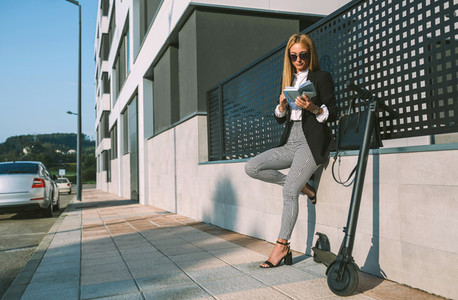 Businesswoman reading notebook with her scooter next