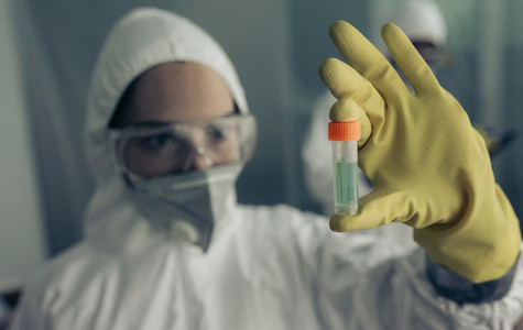 Woman with baceriological protective suit looking at an antidote vial
