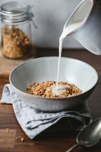 Almond milk is poured in a ceramic bowl with baked granola  Healthy vegetarian breakfast