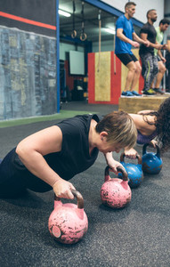 Sportswomen doing push ups with kettlebells