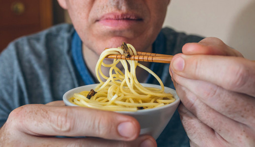 Unrecognizable man eating spaghetti with crickets