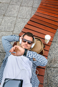 Man with headphones and tablet looking time on his watch