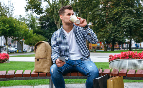 Man with mobile drinking coffee sitting on a bench