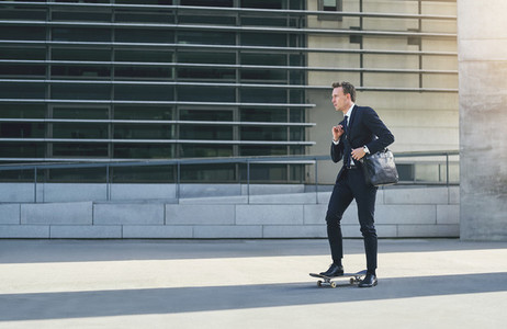 Businessman on skateboard adjusting his shoulder bag