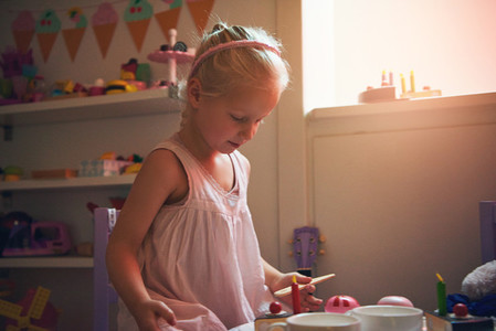 Girl playing tea party looking at toy cake