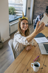 Businesswoman taking selfie with unicorn headband