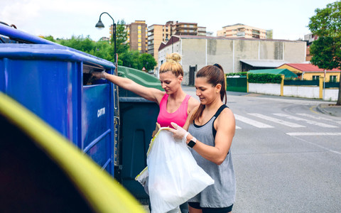 Girls throwing garbage to recycling dumpster
