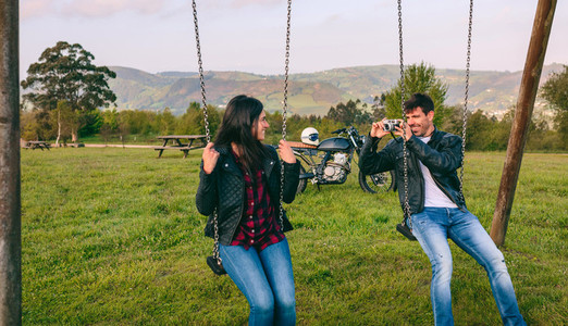 Young man taking a picture of his girlfriend on the swings