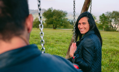 Happy young woman looking camera sitting on a swing