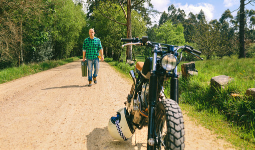 Man with gasoline can walking to custom vintage motorbike